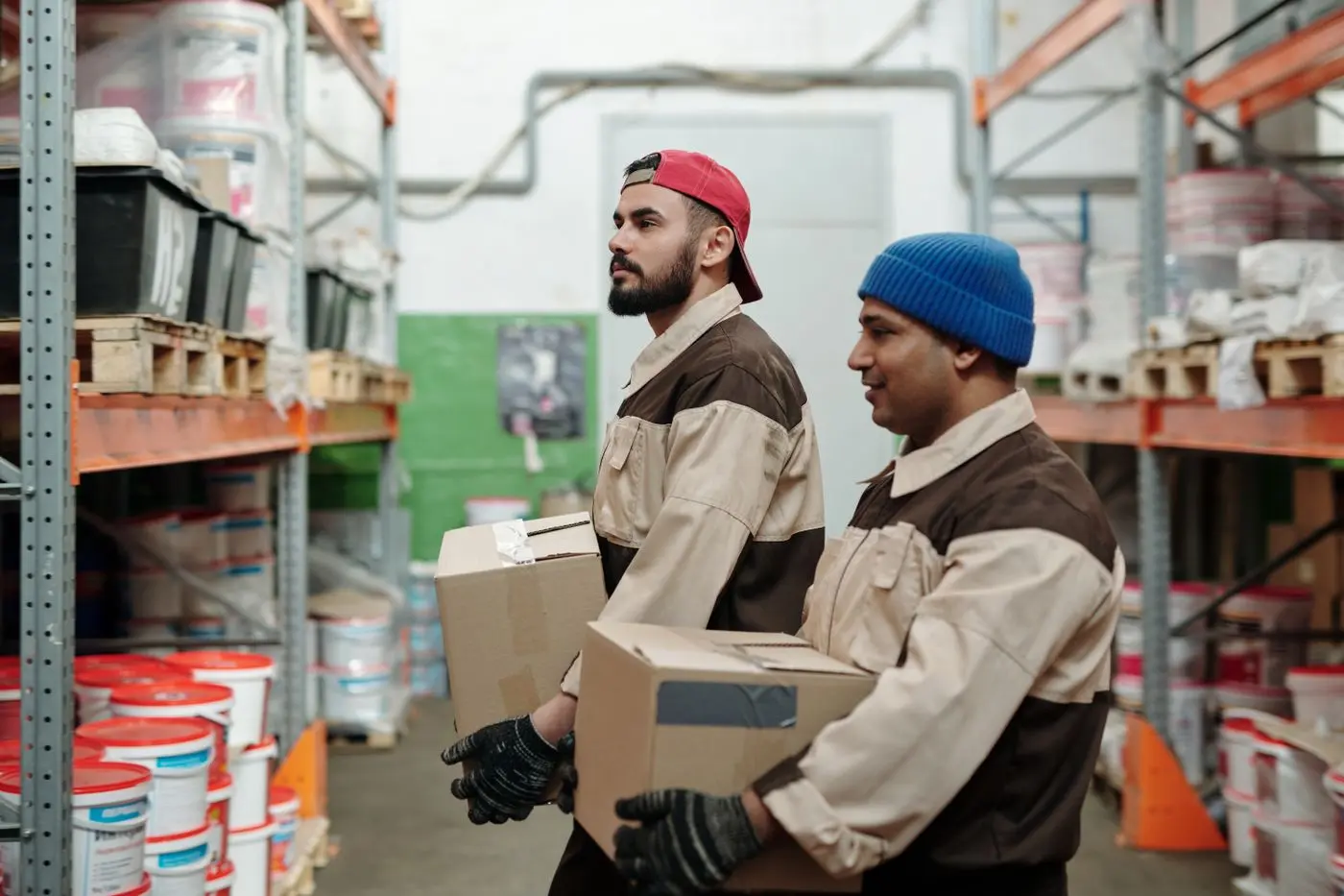 Two warehouse workers carrying stock through an aisle.